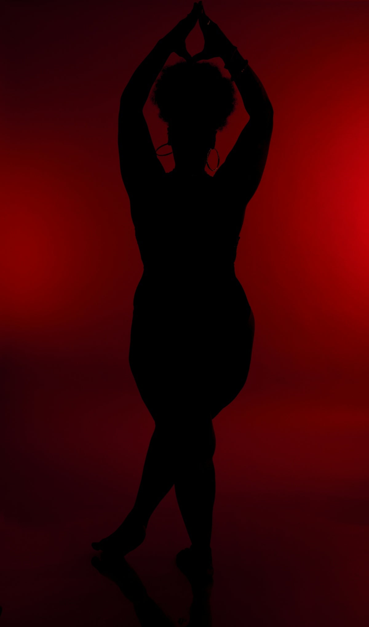 a silhouette of a woman doing yoga in front of a red background