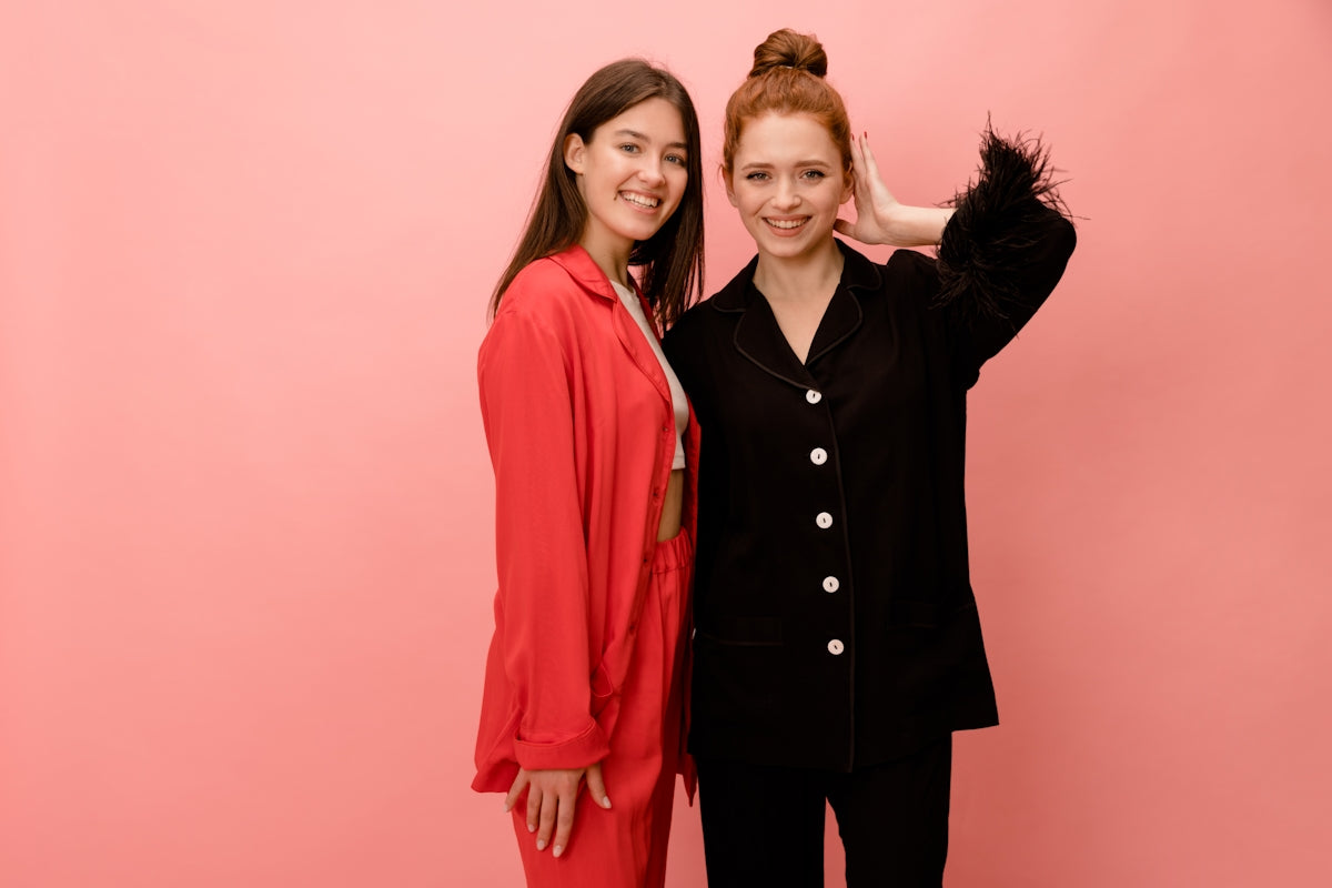 two women standing next to each other in front of a pink wall
