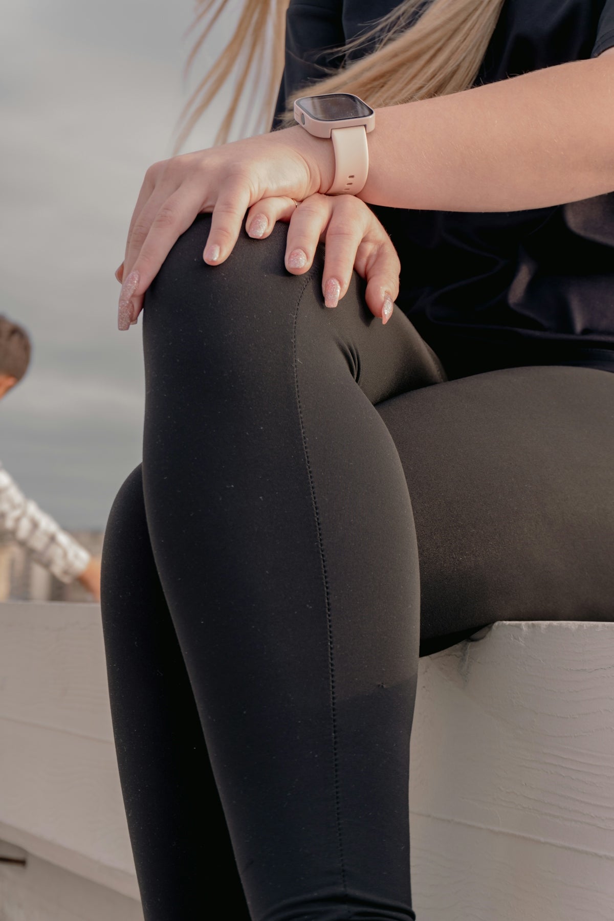 Woman in black leggings and smartwatch sits outdoors.