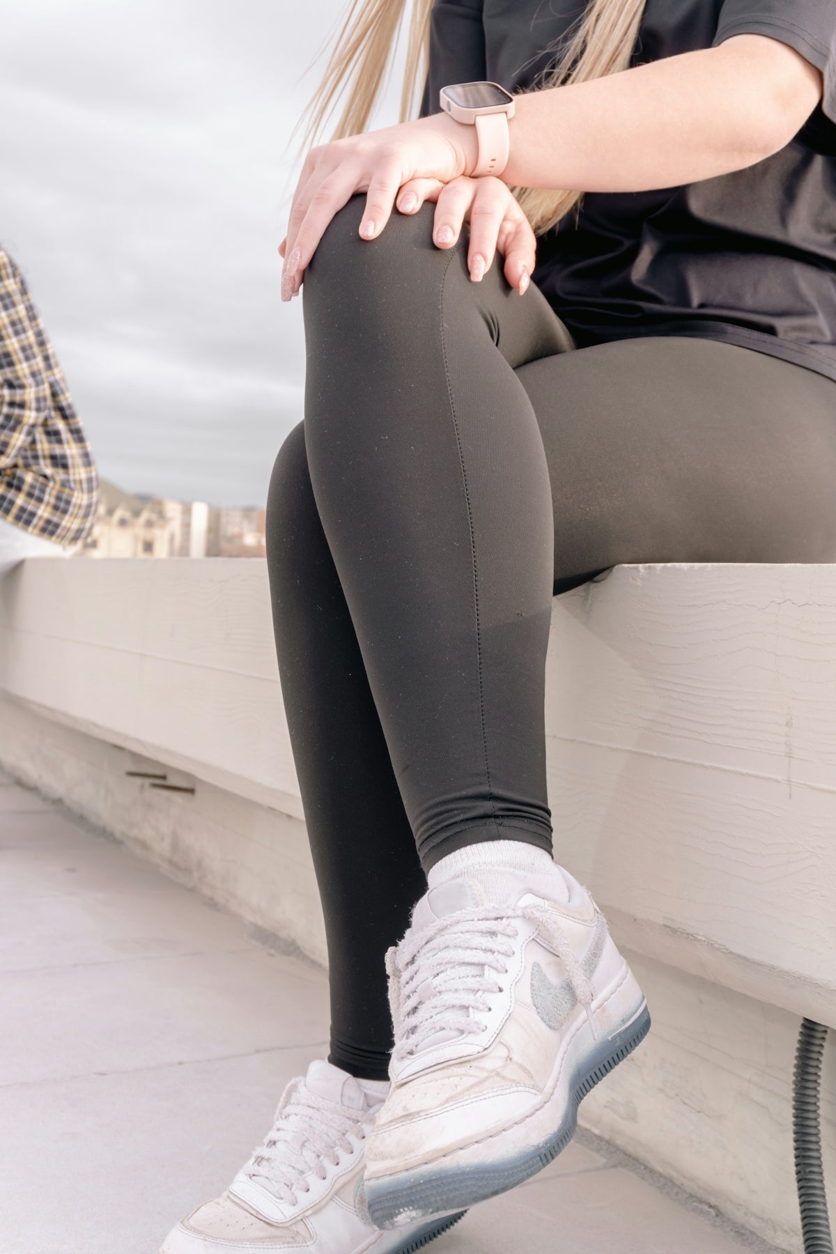 Woman in dark leggings and white sneakers sitting.